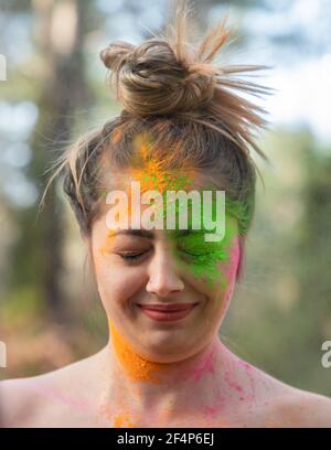Young attractive woman at the Holi color festival of paints in park. Having fun outdoors. Multi Colored powder colors the face. Close Up portrait. Stock Photo