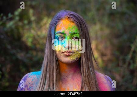 Young attractive woman at the Holi color festival of paints in park. Having fun outdoors. Multi Colored powder colors the face. Close Up portrait. Stock Photo