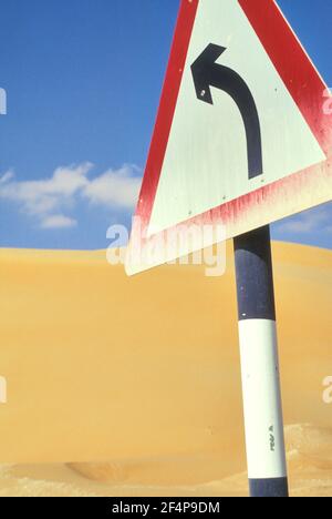 Traffic sign with black curved arrow, sand dunes and blue sky in the background, United Arab Emirates Stock Photo