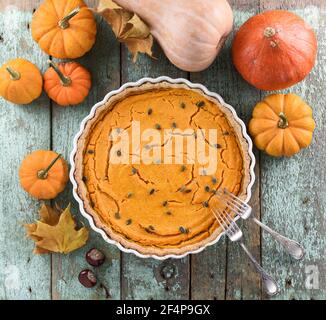 Traditional American open pumpkin pie with pumpkin seeds decorated with small orange pumpkins on shabby robin egg blue background above view Stock Photo