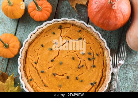 Big open pumpkin pie with pumpkin seeds for Thanksgiving served with small bright orange pumpkins and marple leaves on blue background above view Stock Photo