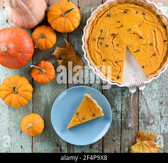 Homemade American pumpkin pie with pumpkin seeds decorated with bright orange pumpkins on shabby robin egg blue background above view Stock Photo