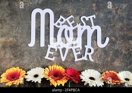 Paper text Best Mom Ever. Greeting card floral design for Mother's day. Gerberas and white baby breath flowers on dark background. Flower arrangement Stock Photo
