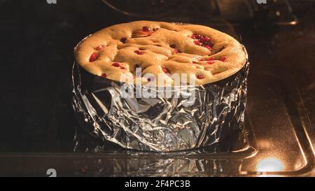 Lingonberry pie with apples is baked in the oven. The berry pie dough rises up. Stock Photo