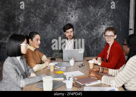 Front view at diverse group of business people meeting at table in black office interior, copy space Stock Photo