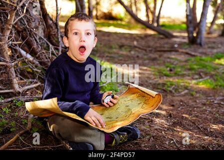 Child with astonished expression to find the location on an old map of a treasure in a forest. Stock Photo