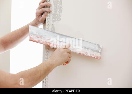 Builder in protective mask using a trowel to add plaster. Plastering wall with putty-knife, close up image. Fixing wall surface and preparation for pa Stock Photo