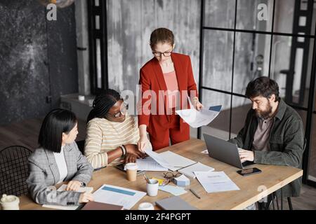 Diverse business team discussing project in black office interior focus on businesswoman wearing red jacket, copy space Stock Photo