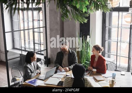 High angle view at diverse business team discussing project at meeting table focus on bearded man smiling at colleagues, copy space Stock Photo