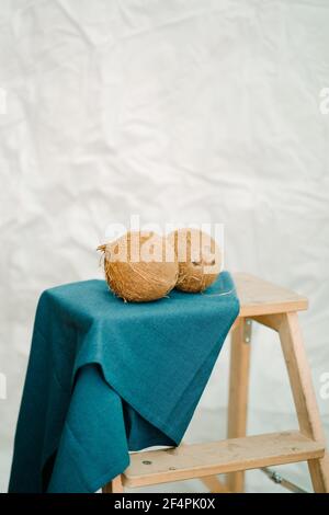 Two organic coconuts over a blue cloth in a wooden stairs and white background Stock Photo