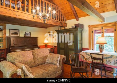 Yellow-brown upholstered fabric sofa, antique wooden rocking chair, green pine wood armoire and upright Howard cabinet grand piano in family room Stock Photo