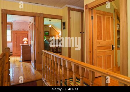 Hallway and opened doors of guest bedrooms and bathroom, maple wood staircase railing on upstairs floor with Eastern Hemlock floorboards in old home Stock Photo