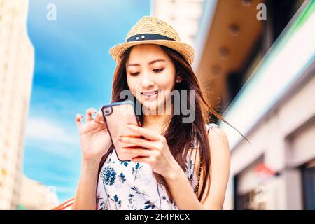 young charming asian woman holding shopping bags ans watching mobile phone on the street Stock Photo