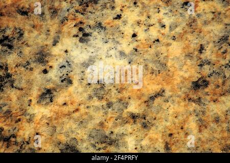 Yellow granite, polished surface of natural stone with black splashes close-up. Background, pattern, texture. Stock Photo