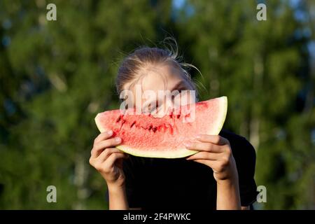 Happy young woman holding ripe juicy slice of watermelon in outdoor on green nature background Stock Photo