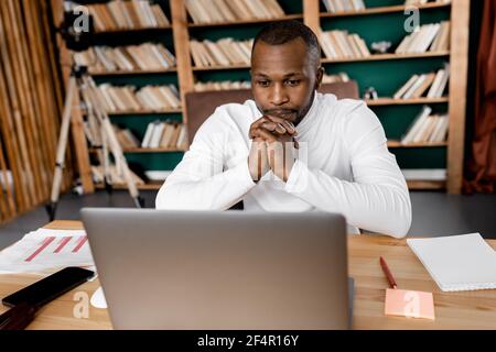 Concentrated male employee sitting at the desk in home office, looking at the laptop screen. Serious businessman thinking about ideas for new project Stock Photo