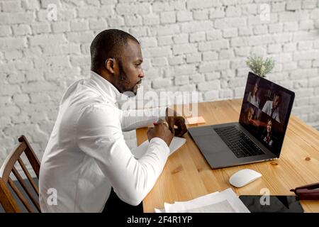 Focused african american male employee is using laptop, having an online video meeting. Serious businessman is working on new project with colleagues Stock Photo