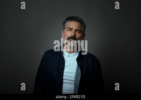 Portrait of a forty year old Caucasian man wearing a denim shirt overlay. Black background, dark concept. Stock Photo