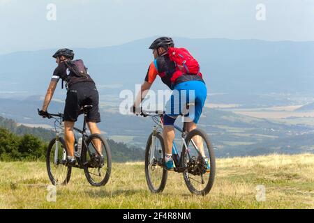 Two men on mountain bikes go down the meadow Active lifestyle people biking friends outdoors cycling backpack Stock Photo