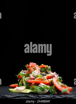 Fresh mixed salad with endive and cherry tomatoes on black plate dining, pouring olive oil Stock Photo