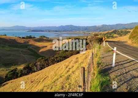 The road into Coromandel township, New Zealand. At the top of the photo is Coromandel Harbour with coastal mussel farms and a fleet of fishing boats Stock Photo
