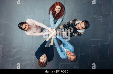 Students putting their hands together and looking up at camera smiling. Multi-ethnic young people with hands stacked together. Stock Photo