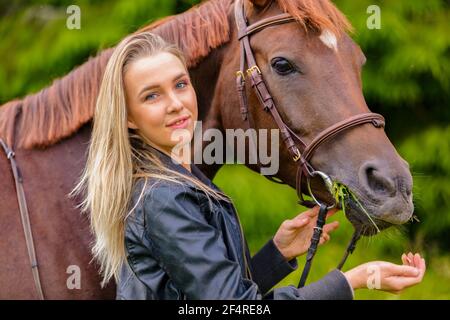 Portrait of a beautiful woman feeding her arabian horse with snacks in the field Stock Photo