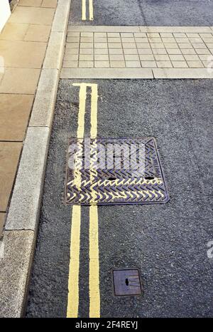 Drain cover with double yellow lines at ninety degrees to lines painted on the road Stock Photo