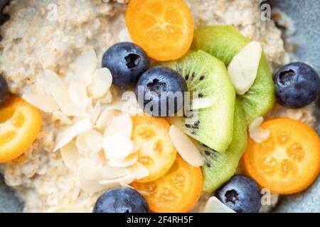 Close up of oatmeal porridge with kumquat, blueberries, kiwi and almond flakes in a bowl. Stock Photo