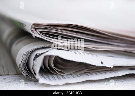 Folded newspapers with almost unreadable Dutch text on a table against plain background with narrow depth of field Stock Photo