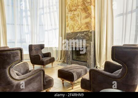 View of stylish living room with fireplace and armchairs around. Interior in brown, beige and golden colors with elements of wood and dark granite. Ro Stock Photo