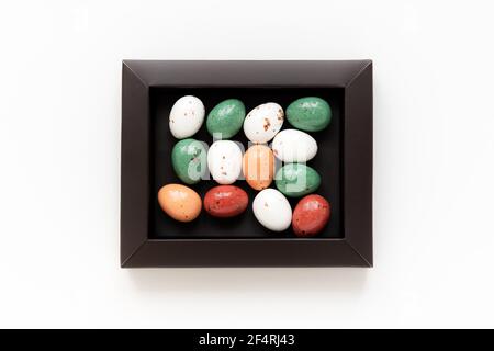 Easter minimal composition with multicolored eggs in a dark box on the white background. Easter concept. Copy space, flat lay. Stock Photo