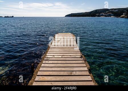 A wood and concrete pier leading out into the clear refreshing waters of the Mediterranean Sea in a picturesque and peaceful cove Stock Photo