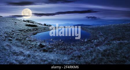 pond on the mountain meadow at night. wonderful summer landscape in full moon light. grass and trees on the hills. ridge in the distance. beautiful wi Stock Photo