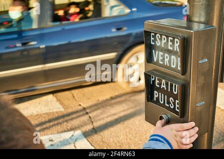 Traffic light button operated by a child who wants to cross the street safely while a car passes through a zebra crossing Stock Photo