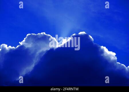 Silver lined cumulus cloud against deep blue sky and sunbeam Stock Photo