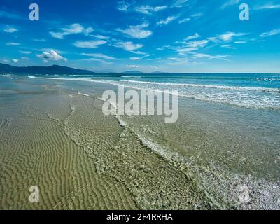 Tropical vacation concept. Soft long waves on the tropical shore of a long empty sea beach. beach with calm waves. Sea foam, blue sky with white cloud Stock Photo