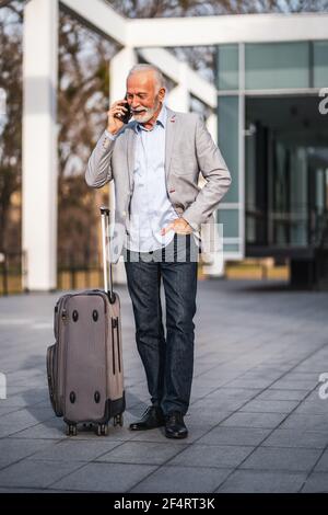 Happy senior businessman is arriving from business trip. He is talking on phone. Stock Photo
