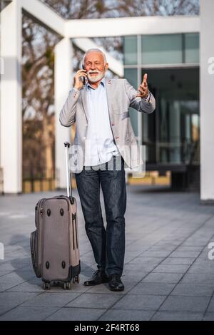 Happy senior businessman is arriving from business trip. He is talking on phone. Stock Photo