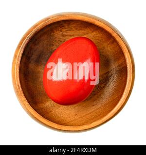 Red dyed Easter egg in a wooden bowl. Hard boiled, colorful dyed chicken egg. Edible Paschal egg, ready to eat, or for an Easter egg hunt. Close-up. Stock Photo
