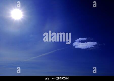Multi star sun and single white cloud against deep blue sky and contrail Stock Photo