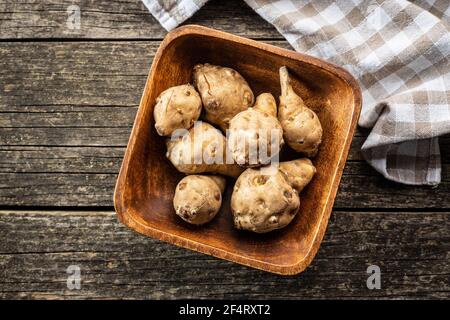 Raw jerusalem artichoke. Topinambur vegetable root in wooden bowl. Top view. Stock Photo