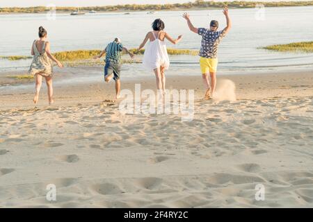 back view of young friends playing and having fun while running and jumping on the beach on vacation. summer activity. friendship, fun and unity conce Stock Photo