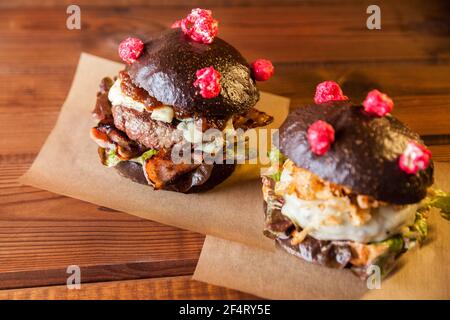 Corona (antiCOVID) burgers with black bun, bacon and cheese on baking paper on a dark wooden table. Burgers are on baking paper. Restaurant, cafe. Stock Photo