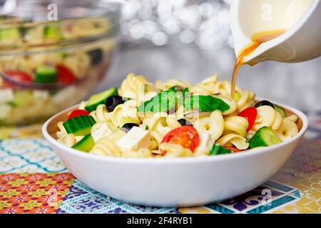 Mediterranean style pasta salad with fresh vegetables and vinaigrette being poured over Stock Photo