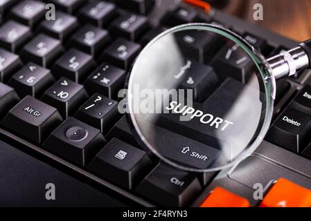 Magnifying glass on key support for black computer keyboard. Technical support. Stock Photo
