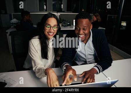 Diverse happy business colleagues sitting together looking and pointing on laptop screen in modern office Stock Photo