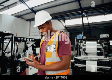 Factory employee checking portable device while examining machinery in industry Stock Photo