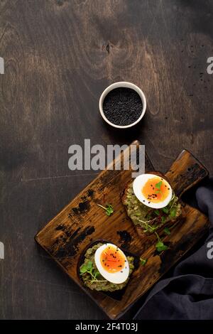 Healthy sandwich with avocado, eggs and microgreens on toast on a serving plate for breakfast. Healthy nutrition dietary concept. Top view Stock Photo