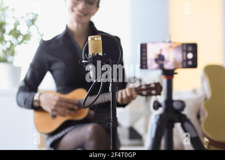 Woman sitting with microphone and holding ukulele in front of camera closeup Stock Photo